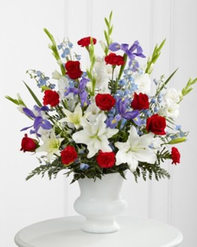 <p>When words fall short, let flowers speak a heartfelt tribute. This arrangement stands as a bold and beautiful gesture of appreciation for a life marked by service, courage, or unwavering dedication. Its patriotic palette of red, white, and blue creates a powerful visual salute honoring a hero’s legacy.</p>
<p>The bouquet features white lilies, deep red roses, and striking blue delphinium and irises, each bloom chosen to represent purity, love, and remembrance. The lilies may arrive in bud form, symbolizing life continuing to unfold and offering renewal and reflection as they bloom in the days ahead.</p>
<p>Expertly designed in a sturdy, neutral-toned container, this arrangement brings strength and elegance to any memorial setting. Its tall and lush composition is ideal for funeral services, military remembrances, or veteran tributes. Whether displayed near the altar, urn, or photo display, it offers a comforting reminder of bravery and devotion.</p>
<p>Each arrangement is handcrafted with care and precision. Same-day local delivery is available, with coordination through funeral homes to ensure fresh and timely arrival. Every detail matters when honoring a life well lived, and this arrangement helps you express gratitude with dignity.</p>
<p>This meaningful tribute shows respect, commemorates service, and shares sympathies during loss. Its classic design and rich symbolism provide comfort, pride, and a lasting impression for those mourning a deeply cherished loved one.</p>