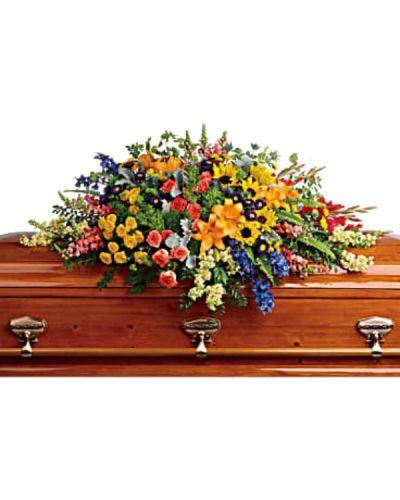 <p>Celebrate the spirit of someone who brought joy, light, and color to the world with this vivid and uplifting casket spray. This floral display honors a vibrant personality and offers a rainbow of hope and comfort to those in mourning. Filled with rich textures and a full spectrum of hues, it serves as a striking tribute that reflects a life filled with warmth, laughter, and unforgettable memories.</p>
<p>This expertly crafted spray overflows with an array of fresh, seasonal blooms. Green hydrangea creates a lush foundation, accented by orange roses, yellow spray roses, and large golden sunflowers that radiate brightness and cheer. Red gladioli and orange snapdragons add height and energy, while blue delphinium and blue eryngium bring cool contrast and serenity. Light yellow stock and purple matsumoto asters introduce softness, with yellow button spray chrysanthemums and green trick dianthus lending playful texture. The entire design is completed with bupleurum, dusty miller, and rich greenery for a natural, garden-inspired finish.</p>
<p>Perfect for funeral services, celebrations of life, or memorial gatherings, this arrangement speaks to the beauty and vibrancy of the person being remembered. Each flower is chosen to represent elements of joy, strength, peace, and remembrance, creating a balanced tribute that brings both color and comfort to a solemn moment.</p>
<p>Each casket spray is handcrafted with care and attention to detail to ensure freshness and elegance. Same-day delivery is available to funeral homes, places of worship, and private residences, ensuring your tribute arrives beautifully arranged and on time.</p>
<p>Include a personal note of condolence at checkout to accompany this meaningful tribute. Honor your loved one with flowers that speak from the heart and bring comfort during life’s most tender moments.</p>