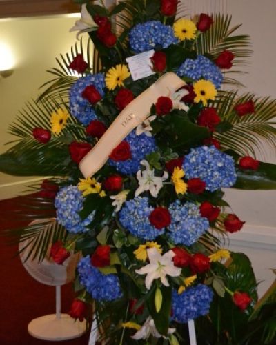 <p>When words are not enough, a floral tribute can express the depth of love, loss, and remembrance with quiet strength. This standing spray offers a dignified and graceful way to honor a cherished life. Thoughtfully designed to bring comfort during moments of farewell, it conveys deep respect and heartfelt emotion through color, structure, and presence.</p>
<p>Bold red roses form the heart of the design, symbolizing enduring love and devotion. Calming blue flowers add depth and serenity, while fresh white blooms provide a sense of peace and purity. The surrounding greenery creates a natural frame, enhancing each element and bringing the entire arrangement to life with texture and fullness. The blend of red, white, and blue results in a balanced tribute that feels both solemn and uplifting, making it especially meaningful when honoring someone deeply admired.</p>
<p>This standing spray is ideal for memorial services, funerals, wakes, and celebration of life gatherings. Its tall, vertical presentation stands beautifully beside a casket, altar, or photo display, serving as a focal point that speaks volumes without a word. Supported by a sturdy easel stand, the arrangement ensures your message of sympathy is seen and felt by all in attendance.</p>
<p>Each spray is thoughtfully crafted with fresh, high-quality blooms arranged for visual harmony and emotional impact. The combination of bold and gentle tones allows this tribute to resonate across generations, relationships, and settings. Whether remembering a veteran, a loved one with quiet strength, or someone cherished beyond measure, this floral display offers a lasting symbol of appreciation and remembrance.</p>
<p>Let this standing spray reflect the legacy of a life well-lived. With its heartfelt presence and meaningful design, it brings comfort, honors memory, and offers peace to those who mourn. It stands not only as a floral gesture but as a visual embrace of love and loss.</p>