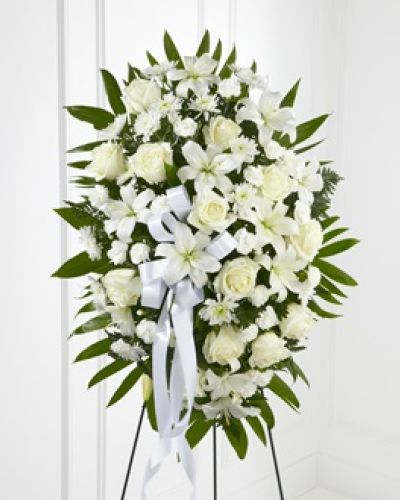 <p>Honor a life of grace and dignity with this beautiful standing spray, a heartfelt expression of sympathy that captures serenity and purity. This all-white arrangement symbolizes peace, remembrance, and eternal love.</p>
<p>The elegant spray features pristine white roses, Asiatic lilies, chrysanthemums, and miniature carnations, carefully arranged to convey gentle strength and timeless beauty. The blooms are nestled among emerald palm fronds and lush greenery, adding depth and natural movement. A white satin ribbon ties the design together with a quiet, graceful finish.</p>
<p>Mounted on a traditional wire easel, this tribute stands tall and dignified at memorials, funerals, or celebrations of life. Its shape and scale offer a striking presence near the casket, altar, or entryway. Designed to comfort and uplift, it serves as a visual expression of love and a meaningful way to pay respects.</p>
<p>Every arrangement is handcrafted with precision and compassion. Same-day local delivery is available, with close coordination with funeral homes to ensure timely, respectful presentation. When words are not enough, flowers speak gently on your behalf.</p>
<p>Let this standing spray deliver a message of peace, reverence, and support. Whether sending love from near or far, it provides a graceful and dignified way to honor a cherished life.</p>