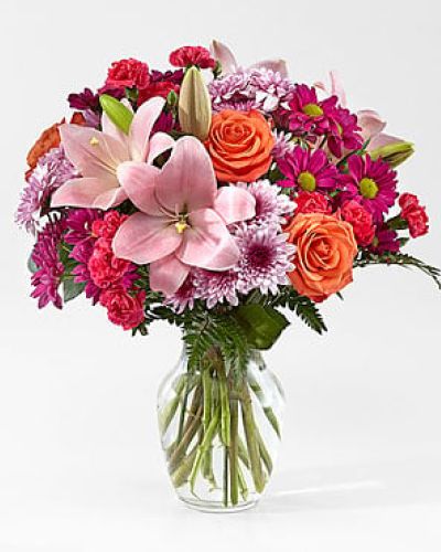 <p>Some people light up your world—and this bouquet is a radiant way to show them just how much they mean. Bursting with vibrant color and heartfelt energy, it’s a joyful expression perfect for brightening anyone’s day.</p>
<p>Pink lilies take center stage with their graceful, star-shaped blooms, surrounded by vivid orange roses, bold hot pink carnations, soft lavender cushion poms, and touches of fresh greenery. The result is a lively arrangement full of warmth, gratitude, and affection, making it suitable for everything from birthdays to just-because moments.</p>
<p>This bouquet is a thoughtful gift for friends, family, or that special someone. Its rich color palette and uplifting design make it an easy choice for thank-yous, anniversaries, or anytime you want to say “you matter.”</p>
<p>Expertly handcrafted by a local florist, each arrangement is delivered in a classic clear glass vase and filled with fresh, high-quality blooms. While flower varieties may change slightly based on seasonal availability, the bouquet’s joyful spirit remains consistent.</p>
<p>Celebrate life’s bright spots with a bouquet that reflects the joy of connection and the beauty of shared moments.</p>