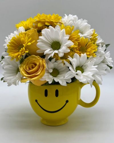 <p>Sometimes the simplest gesture makes the biggest difference—and the Smile Mug Bouquet is pure sunshine in a cup. Bursting with cheerful yellow roses and soft white blooms, all arranged in a classic smiley-face mug, this joyful gift is designed to brighten anyone’s day. Whether you're offering encouragement, saying thanks, or just sending a little love, it’s sure to deliver a smile.</p>
<p>At the heart of the design are radiant yellow roses, long associated with friendship, optimism, and positivity. Crisp white flowers add softness and balance, enhancing the fresh, uplifting vibe. The arrangement comes nestled in a reusable ceramic mug adorned with a bright yellow smiley face—a fun keepsake they’ll enjoy long after the blooms are gone.</p>
<p>Perfect for any uplifting occasion, this bouquet makes a thoughtful “get well soon” gift, a heartfelt pick-me-up, or a charming “thinking of you” surprise. It's also great for birthdays, thank-you gestures, or brightening up an office desk. With its compact size and sunny disposition, it fits anywhere and fills the space with warmth and good vibes.</p>
<p>Each arrangement is handcrafted by skilled florists using the freshest blooms available. Local delivery is available through our trusted florist network, ensuring timely arrival and careful presentation. Some flowers may arrive in bud form to extend the joy as they bloom.</p>
<p>The Smile Mug Bouquet is more than a floral gift—it’s a little burst of happiness that keeps on giving.</p>
