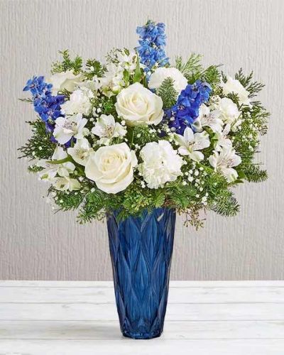 <p>Bring a touch of winter elegance into any space with the Holiday Radiance Bouquet—a luminous arrangement that captures the crisp beauty of the season. With its cool tones and graceful florals, this sophisticated design offers a serene and festive way to celebrate or send seasonal cheer.</p>
<p>This refined bouquet features a harmonious blend of snowy white blooms and fresh greenery, accented by soft blue flowers that evoke the charm of a wintry landscape. White roses and lilies contrast beautifully with seasonal evergreens and touches of blue delphinium or hydrangea, creating a clean, luxurious look. A tall blue glass vase adds height and drama, reflecting the icy tones of the flowers and lending the arrangement a polished, modern finish.</p>
<p>Perfect for winter holidays, New Year celebrations, or simply sending a peaceful message, the Holiday Radiance Bouquet offers a refreshing alternative to traditional red-and-gold holiday décor. Its calming color palette and elegant design make it ideal for brightening entryways, adorning tablescapes, or expressing seasonal sentiments with understated style.</p>
<p>Each bouquet is handcrafted by expert local florists using the freshest seasonal blooms. Some flowers may arrive in bud form to extend their beauty and ensure lasting enjoyment. Local delivery is available to guarantee your gift arrives fresh, artfully arranged, and ready to impress.</p>
<p>Send the Holiday Radiance Bouquet today and share the quiet beauty of the season through a glowing expression of peace, elegance, and winter wonder.</p>