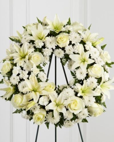 <p>Offer a heartfelt gesture of sympathy with a timeless wreath that radiates serenity and quiet strength. This elegant design is a graceful way to express lasting love and support during times of loss, with its circular form symbolizing eternity and the unbroken bond of cherished memories.</p>
<p>A thoughtful mix of white roses, Asiatic lilies, mini carnations, and cushion poms creates a soothing palette that brings peace and comfort. Each flower is carefully chosen for its meaning—roses for reverence, lilies for renewal, and carnations for devotion. The arrangement is accented with lush greenery, giving the wreath structure and depth while enhancing its natural beauty.</p>
<p>This all-white wreath is especially suited for memorial services, funeral gatherings, and graveside tributes. Its gentle hues and traditional shape offer a dignified expression of condolence, providing a quiet moment of reflection and remembrance. Whether honoring a loved one, friend, or colleague, this design brings comfort and grace to solemn occasions.</p>
<p>With its harmonious blend of blooms and balanced composition, the wreath stands as a lasting tribute to a life well lived. The floral selections evoke purity and hope, helping to communicate emotions when words are difficult to find. Its versatile size and classic styling make it appropriate for a wide range of settings and traditions.</p>
<p>Every wreath is handcrafted with fresh flowers and foliage, making each one a unique and meaningful creation. While specific blooms may vary due to seasonal availability, the spirit of the design remains consistent—offering peace, remembrance, and heartfelt sympathy with beauty and care.</p>