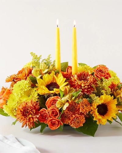 <p>Celebrate the warmth and wonder of fall with the Autumn Harmony Centerpiece—a rich, radiant floral arrangement designed to bring people together. Whether you're hosting a harvest dinner, expressing gratitude, or adding festive charm to your own table, this seasonal centerpiece sets the perfect tone with its inviting colors and glowing candlelight.</p>
<p>This deluxe arrangement features a vibrant mix of autumn favorites, including golden sunflowers, burnt orange roses, crimson mums, and deep red carnations. Fresh autumn greens provide a lush base, while rustic accents like fall leaves, berries, and sprigs of eucalyptus add texture and charm. At the center, glowing taper candles offer warmth and ambiance, turning any meal into a cozy celebration.</p>
<p>Perfect for Thanksgiving, Friendsgiving, seasonal gatherings, or simply as a thoughtful gift, the Autumn Harmony Centerpiece captures the colors and comforts of fall. Its low, full design ensures easy conversation around the table, while the bold seasonal palette reflects the richness of falling leaves, crisp evenings, and heartfelt traditions.</p>
<p>Each centerpiece is carefully handcrafted by local florists using the freshest blooms available. Some flowers may arrive in bud form to ensure longevity and extended beauty. Local delivery is available to guarantee your gift arrives fresh, festive, and ready to enjoy.</p>
<p>Send the Autumn Harmony Centerpiece today and share the spirit of the season through warmth, color, and heartfelt connection.</p>