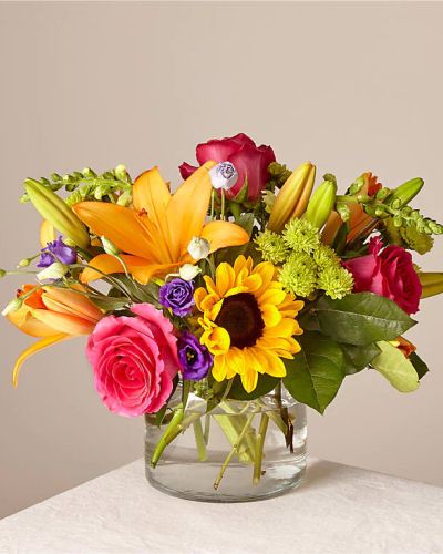 <p>Celebrate life’s brightest moments with a bouquet that radiates happiness, color, and uplifting energy. This cheerful arrangement is designed to bring joy to any day, offering a vibrant mix of blooms that feels like a celebration in floral form. Whether for a birthday, a moment of encouragement, or a spontaneous surprise, it delivers beauty with bold personality.</p>
<p>The bouquet features sunny sunflowers, hot pink roses, purple double lisianthus, orange LA Hybrid lilies, yellow snapdragons, green button poms, and fresh greenery. Each bloom is carefully selected for its vivid color and freshness, creating a dynamic display that catches the eye and lifts the spirit. Arranged in a clear glass vase, the flowers take center stage, letting their natural brilliance shine through with effortless charm.</p>
<p>This design is perfect for sending congratulations, well wishes, or simply letting someone know they’re appreciated. The combination of rich textures and playful colors brings instant cheer to any room, making it a favorite choice for all kinds of occasions. Its versatility and joyful presence make it suitable for friends, loved ones, or anyone who deserves a thoughtful and energetic gesture.</p>
<p>Crafted with care and attention to detail, each arrangement is designed to ensure balance, harmony, and maximum visual impact. From the vibrant hues to the structured flow of the design, everything works together to create a bouquet that feels as meaningful as it is beautiful. It’s a gift that goes beyond aesthetics to express warmth, kindness, and positivity.</p>
<p>Let this joyful bouquet be your way of turning an ordinary day into something special. Bursting with color and full of heart, it brings lasting smiles and leaves behind a memory of happiness that lingers long after the flowers are gone.</p>