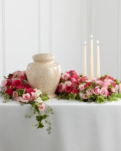 <p>Celebrate a life filled with love and kindness through this beautifully designed floral arrangement that surrounds the urn with elegance and warmth. Created to bring comfort and serenity to a final farewell, this sophisticated tribute honors a loved one with graceful blooms and gentle candlelight.</p>
<p>Fuchsia and pale pink roses, along with matching spray roses, form the heart of the design. These roses are accented with lush greenery and arranged to gently wind around the base of the urn, creating a soft and natural setting that reflects tenderness and care. Three ivory taper candles are nestled within the florals, casting a peaceful glow that adds reverence and calm to the moment.</p>
<p>Ideal for memorials, celebration of life services, or cremation ceremonies, this arrangement highlights the urn with beauty and meaning. Its circular form symbolizes eternal love, while the combination of color and candlelight creates a comforting atmosphere for friends and family.</p>
<p>Each arrangement is handcrafted with care and made fresh to order, then delivered directly to the funeral home or service location. Timely and respectful presentation is ensured through close coordination with local venues, with same-day delivery available in the area.</p>
<p>Add a personal message during checkout to accompany your tribute with dignity. This arrangement offers a thoughtful way to express love, provide comfort, and honor a life well lived with flowers that speak from the heart.</p>