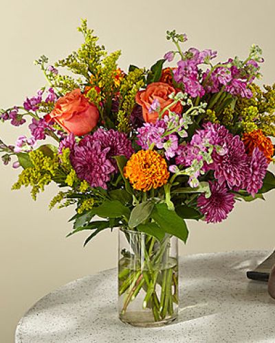 <p>Step into a world of floral enchantment with a bouquet that captures the joy and color of a blooming garden. Radiant and uplifting, this seasonal arrangement brings warmth and charm into any space, turning everyday moments into something a little more magical. It’s the perfect blend of whimsy and elegance, designed to brighten spirits and elevate surroundings.</p>
<p>The bouquet features a cheerful mix of sunshine-yellow lilies, coral roses, lavender stock, and pink carnations. Each bloom is selected for its vibrant hue, lush texture, and seasonal freshness. Accents of soft greenery and playful filler flowers enhance the overall design, creating depth and movement that evoke the feeling of a storybook garden in full bloom.</p>
<p>Arranged in a classic clear glass vase, the design strikes a balance between graceful structure and natural beauty. Its pastel palette and airy composition make it ideal for a variety of spaces—from kitchen tables to office desks to bedside arrangements. The look is versatile and timeless, appealing to both traditional and modern tastes.</p>
<p>This bouquet is a thoughtful choice for birthdays, thank-you gifts, celebrations, or simple acts of kindness. Its bright colors and gentle fragrance bring comfort and joy, making it a welcome addition to any occasion. Whether gifted or kept as a personal pick-me-up, it delivers a meaningful message with grace and style.</p>
<p>Handcrafted by a professional florist using fresh, premium flowers, each bouquet is made to order with care. While exact blooms may vary based on seasonal availability, the overall color harmony and feel will remain beautifully consistent. Share a moment of joy with a floral gift that turns the ordinary into the extraordinary.</p>
