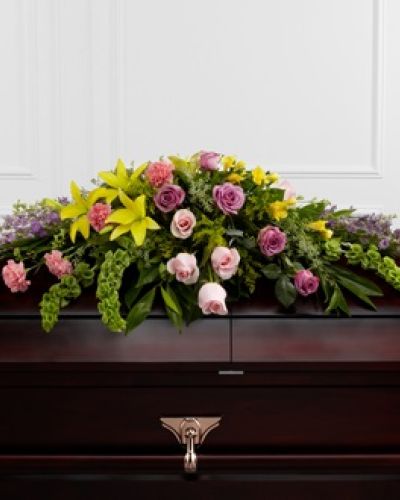 <p>When it is time to say goodbye, a radiant floral tribute offers comfort and beauty during a final farewell. This casket spray presents an elegant expression of enduring love, designed to bring light and peace to a memorial service.</p>
<p>The lush arrangement overflows with a rich variety of blossoms in soft pastels and warm yellows, creating a visual symphony of remembrance. Lavender roses, delicate pink roses, and lavender larkspur evoke affection and serenity, while cheerful yellow Asiatic lilies and golden freesia add a hopeful sense of renewal. Pink carnations, Bells of Ireland, and golden solidago provide texture, depth, and symbolic meaning throughout the design.</p>
<p>Each bloom is carefully placed among fresh greenery to create a generous display that gracefully spans the casket. The blend of colors and flowers reflects the many layers of a life well lived—tenderness, joy, grace, and strength.</p>
<p>This casket spray is ideal for honoring someone known for their gentle heart, vibrant spirit, or devoted nature. It serves as a fitting tribute for a beloved family member or friend who brought warmth and beauty to those around them.</p>
<p>Expertly arranged and delivered with care, this tribute arrives ready to offer a meaningful and heartfelt expression of love and appreciation. It serves as a lasting symbol of cherished memories and provides peace to those left behind.</p>