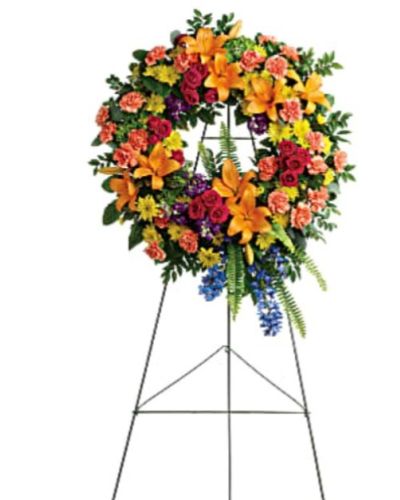 <p>Celebrate the vibrant spirit of a loved one with a radiant floral wreath that reflects the beauty, joy, and warmth they brought to the world. Designed in a full circle to symbolize eternal love and remembrance, this striking sympathy wreath brings comfort to grieving hearts while honoring a life filled with colorful memories.</p>
<p>This uplifting design features green hydrangea, hot pink spray roses, and bold orange Asiatic lilies, blending cheer and grace in every petal. Orange carnations, blue delphinium, and purple stock add depth and contrast, while yellow cushion spray chrysanthemums brighten the arrangement with joyful energy. Accents of huckleberry, variegated pittosporum, sword fern, silver dollar eucalyptus, and lemon leaf create a natural and textured frame. The wreath is presented on a wire easel for display at funeral services, memorials, or celebration of life ceremonies.</p>
<p>Perfect for honoring a beloved family member or friend whose personality was full of light and laughter, this wreath offers a visual expression of love, gratitude, and hope. Its vibrant palette is a gentle reminder that even in times of sorrow, beautiful memories endure.</p>
<p>Each wreath is handcrafted with care by experienced florists to convey sympathy with elegance and dignity. Same-day delivery is available to funeral homes and service locations to ensure your tribute arrives fresh, beautiful, and ready to honor your loved one.</p>
<p>Include a personal message of condolence at checkout to accompany this wreath. Remember those you’ve lost with flowers that speak from the heart. Let love and color surround their memory with this vibrant tribute.</p>