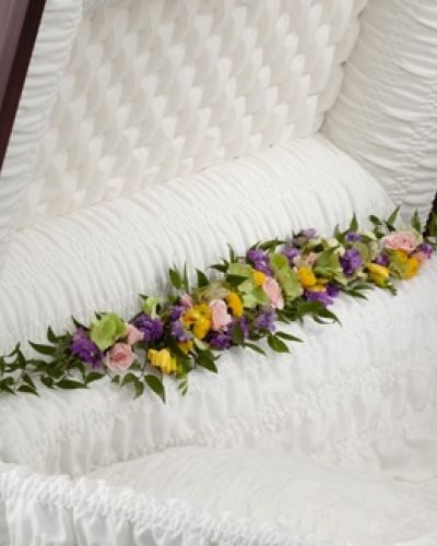 <p>Soft and graceful, this casket adornment offers a delicate way to express love and honor during a final farewell. Designed to rest along the inside edge of the casket, it brings warmth and serenity to the service with its thoughtful presence.</p>
<p>The arrangement features a harmonious blend of colors and textures, combining fresh green hydrangea with the soft charm of pink spray roses. Bright yellow freesia adds cheerful fragrance, while lavender larkspur and yellow button poms provide vertical interest and a nod to nature’s gentle beauty. Expertly arranged to cascade in a natural line, the design evokes a trail of blooms leading from this life into peaceful rest.</p>
<p>More than a floral piece, this adornment symbolizes a pathway of love, guiding the memory of a cherished individual with softness, elegance, and light. Each flower represents qualities such as devotion, joy, and peaceful remembrance, making it especially fitting for someone who walked gently through life and left beauty behind.</p>
<p>Ideal as a complement to larger sprays or standing pieces, this casket adornment suits families who want every detail of the service to reflect love and care. Whether honoring a parent, grandparent, spouse, or close friend, it offers a tender final gesture of grace and beauty.</p>
<p>Carefully arranged and delivered with compassion, this tribute arrives fresh and vibrant, ready to provide a heartfelt and seamless presentation. Let this trail of blossoms serve as a lasting tribute and gentle reminder that love continues to bloom even in farewell.</p>